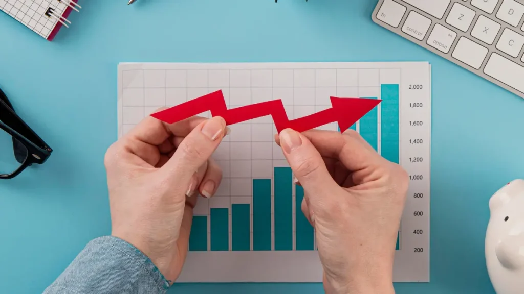 Vista superior de itens de escritório dispostos junto a um gráfico de crescimento, com mãos segurando setas indicando progresso e sucesso.